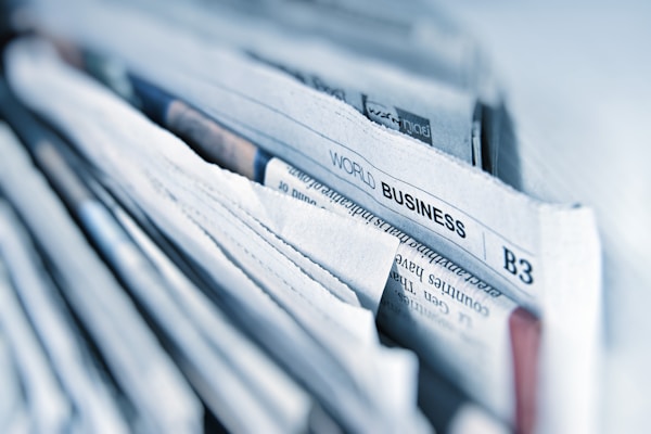 Stacked newspapers with a World Business headline, representing the market trends behind agentic commerce